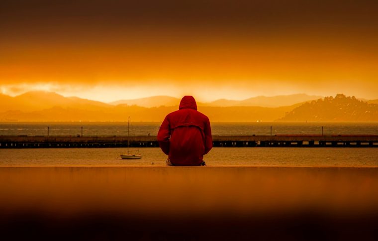 Man with red coat on facing the sea at sunset with his back to the camera